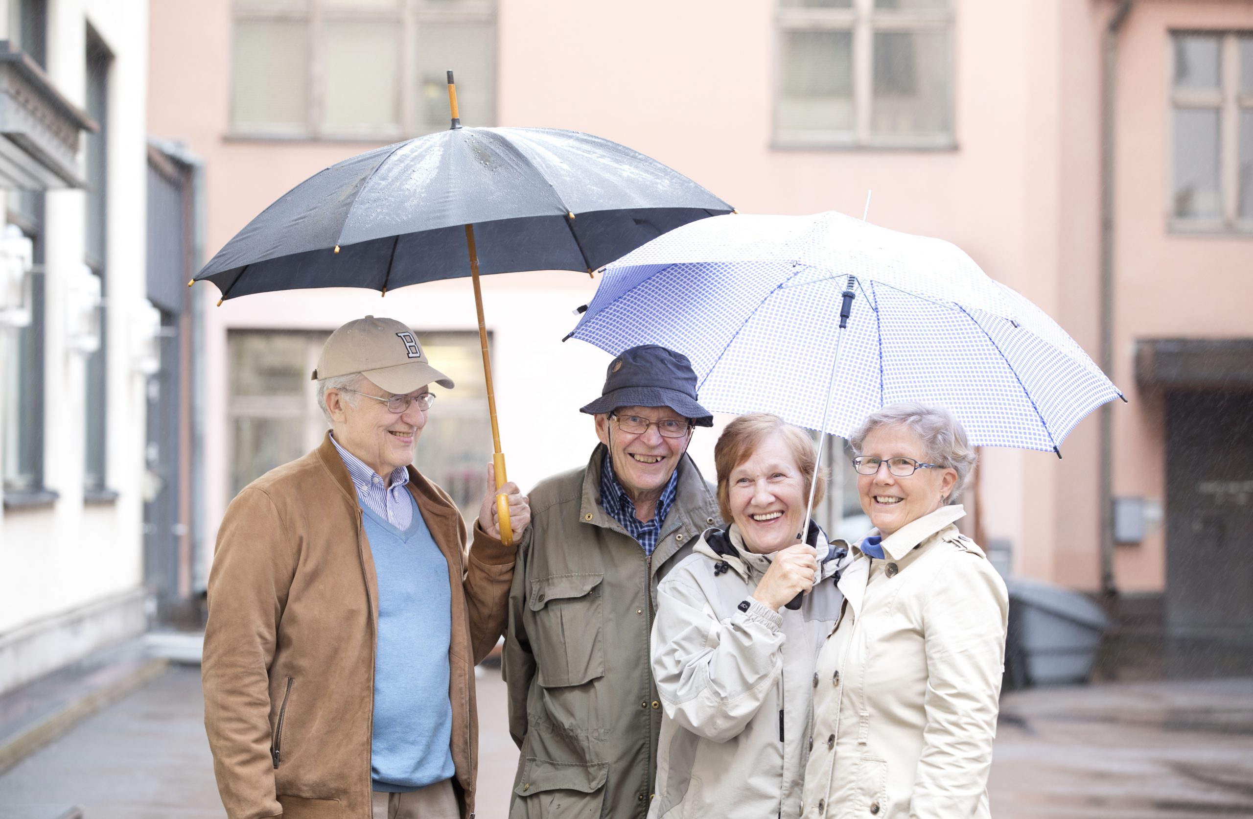 Kaksi miestä ja kaksi naista seisovat sateenvarjojen alla hymyillen